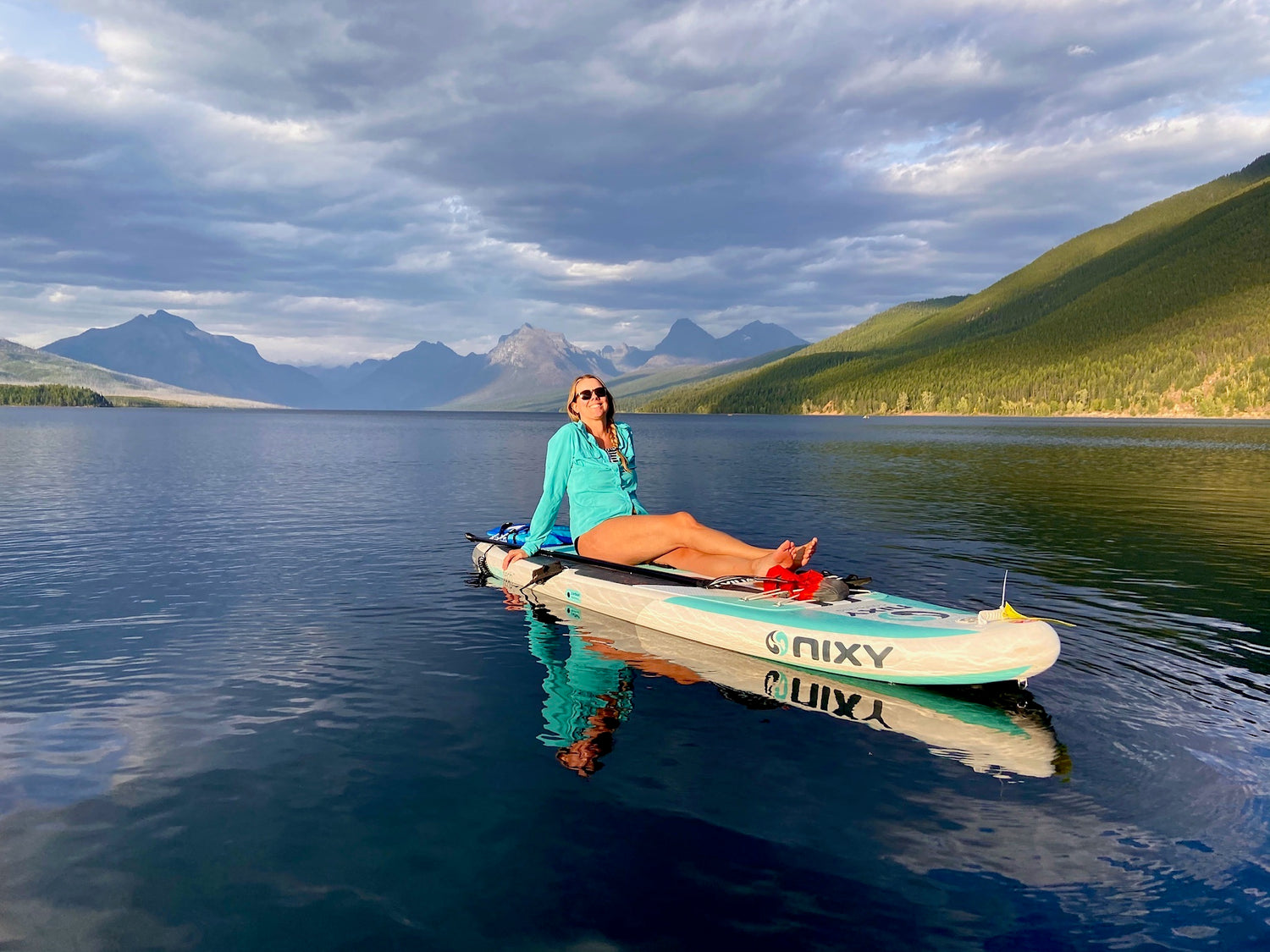 Woman sitting on a standup paddle board surrounded by mountains on Lake McDonald in Glacier National Park. 